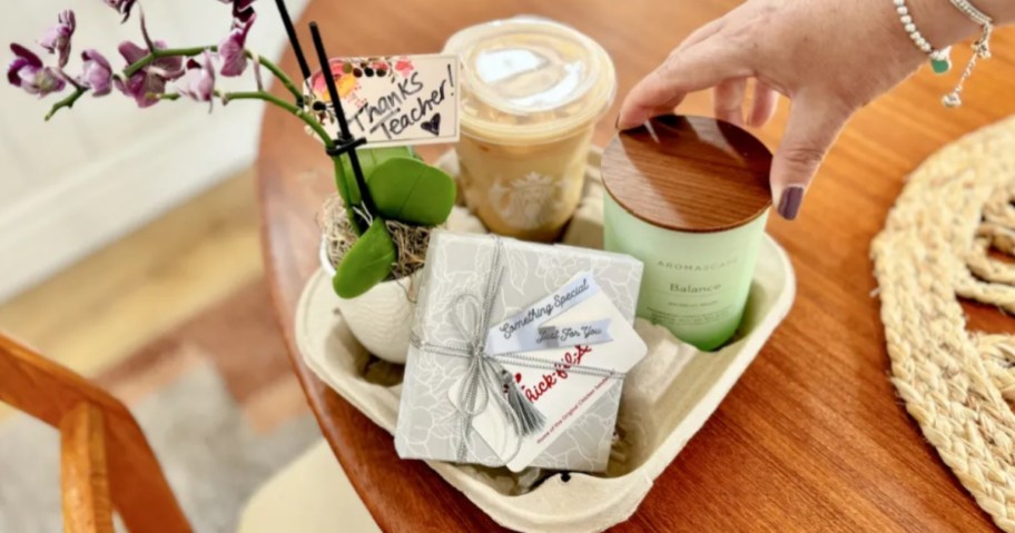 a teacher gift idea in a drink holder container with a candle, Starbucks coffee, an orchid plant, and a card with a Chick-fil-A gift card attached