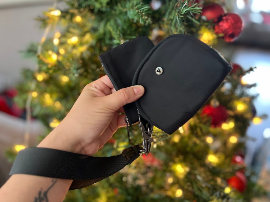 hand holding a black wristlet pouch in front of christmas tree