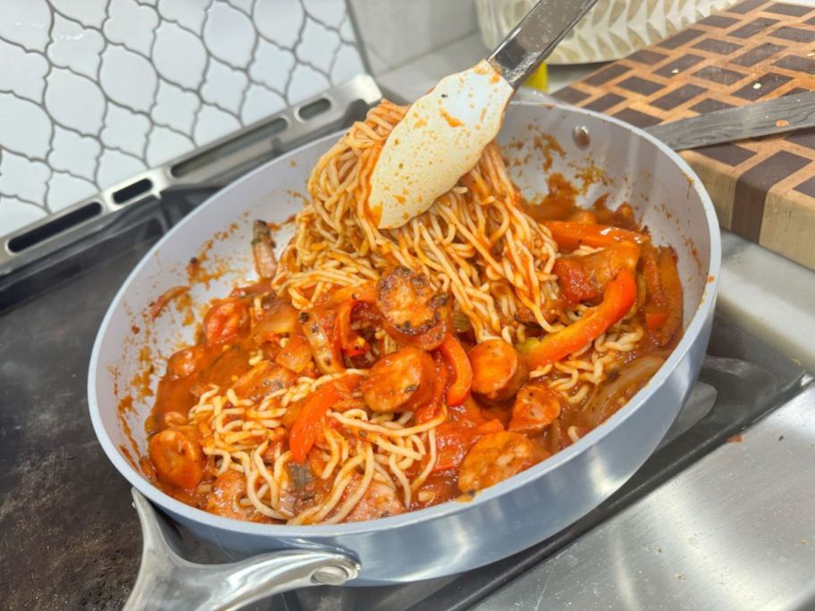 tongs holding up pasta from saute pan with sausage and pepper pasta