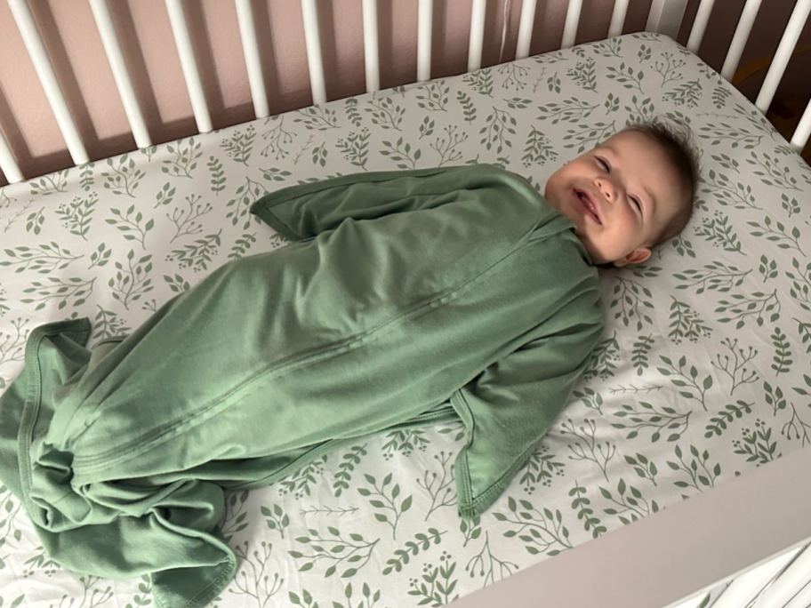 baby laying in crib with green swaddle