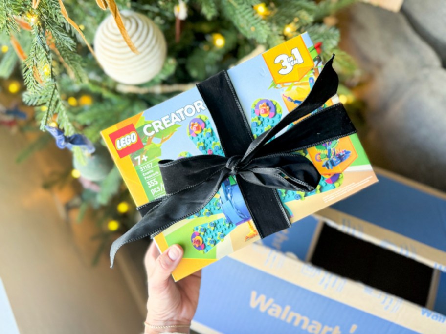 hand holding the lego creator 3-in-1 peacock set all wrapped up in a bow in front of a christmas tree and walmart box