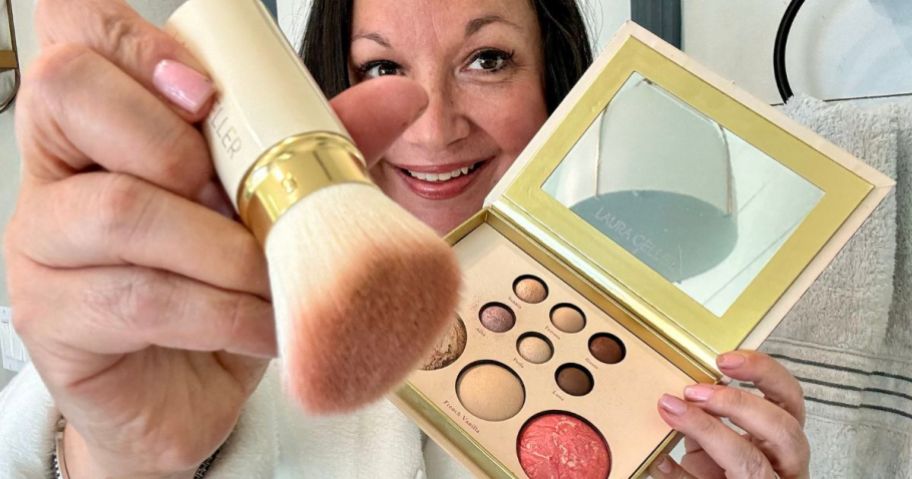 Woman holding a laura Geller makeup kit and kabuki brush