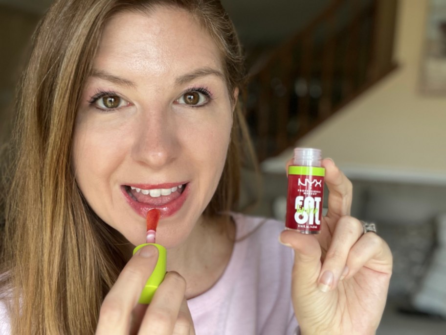 woman applying nyx fat lip oil and smiling at the camera