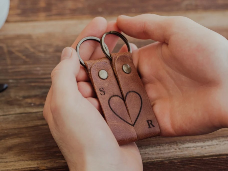 a hand holding a set of leather keychains with a heart and initials on each one