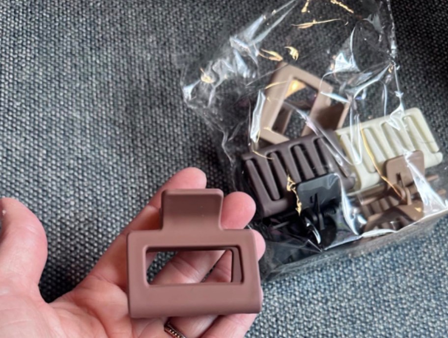 hand holding brown hair clip with bag of clips in background