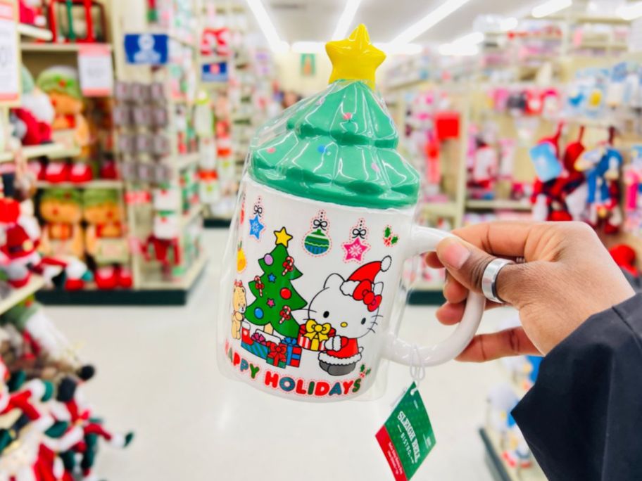 a womans hand holding a hello kitty holiday coffee mug