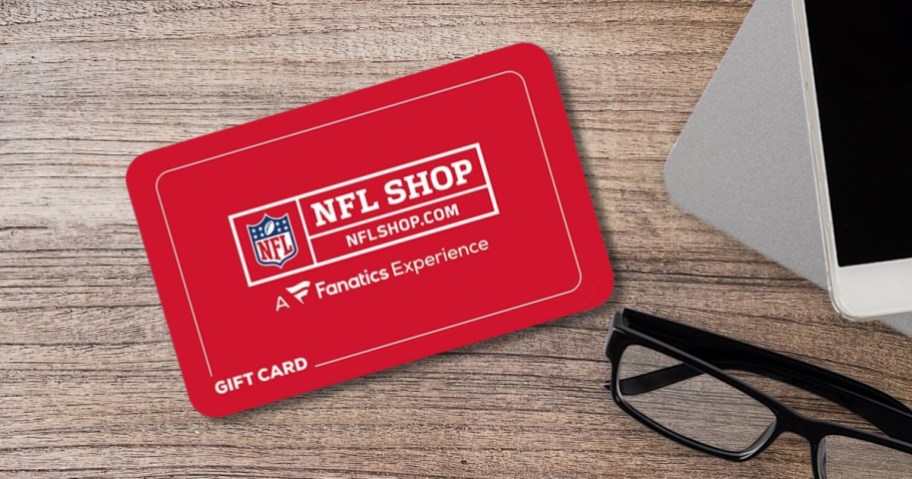 a red Fanatics NFLShop.com Gift Card on a desk - part of a pair of black framed glasses and a white smartphone are off to the side 