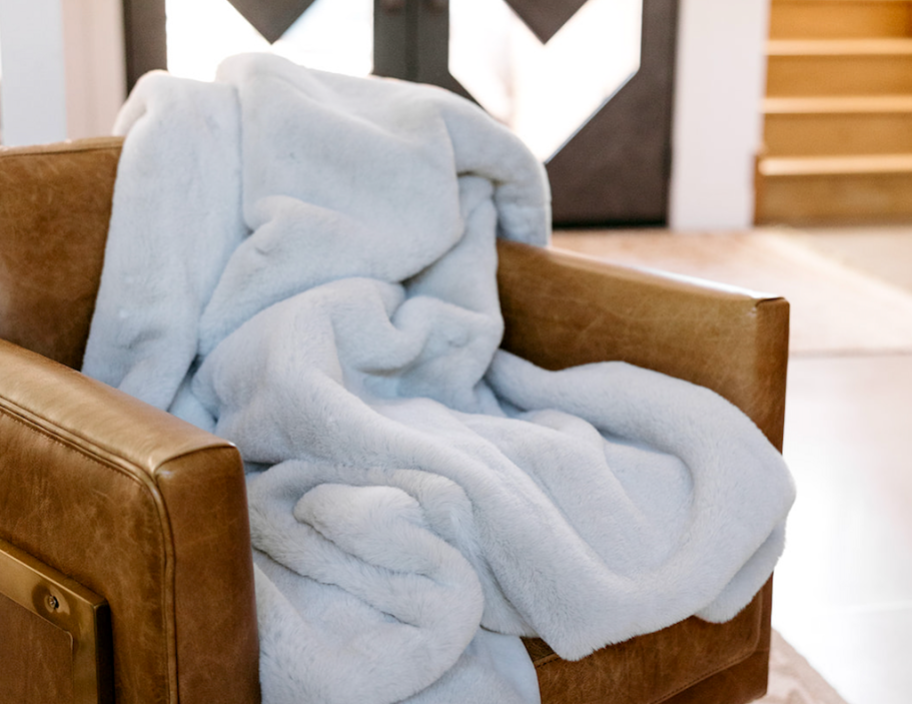 a plush faux fur light cream color blanket on a brown leather side chair