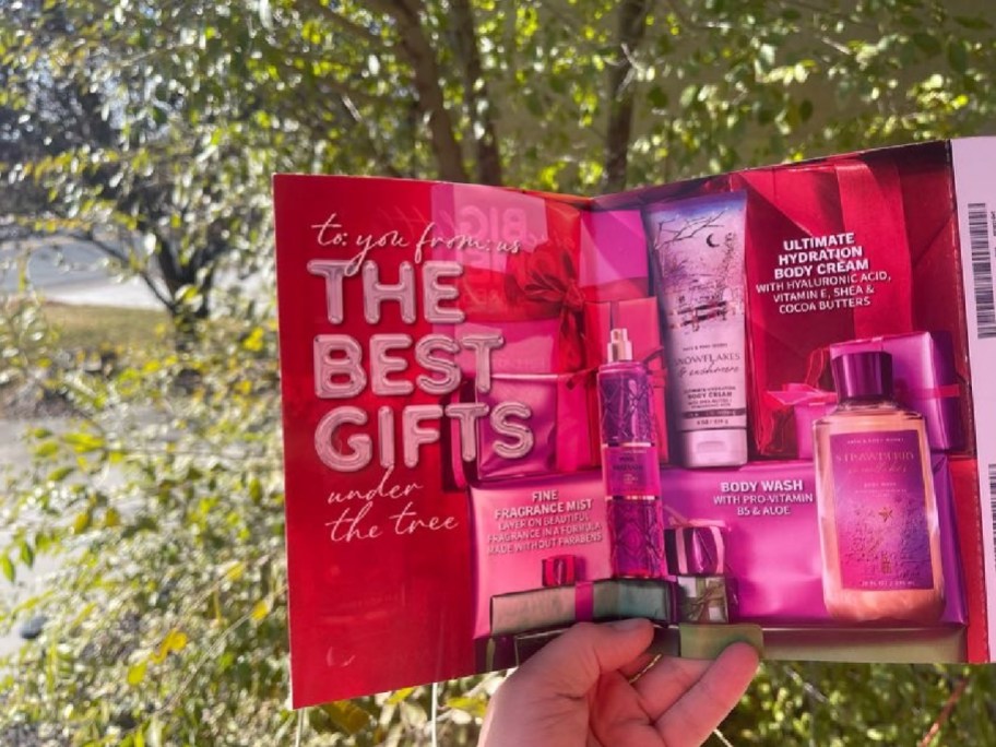 bath and body works coupon mailer held in hand in front of trees