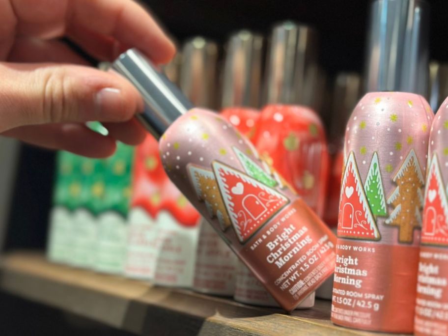 Hand grabbing a bottle of Bath & Body Works Bright Christmas Morning Room Spray off a store shelf