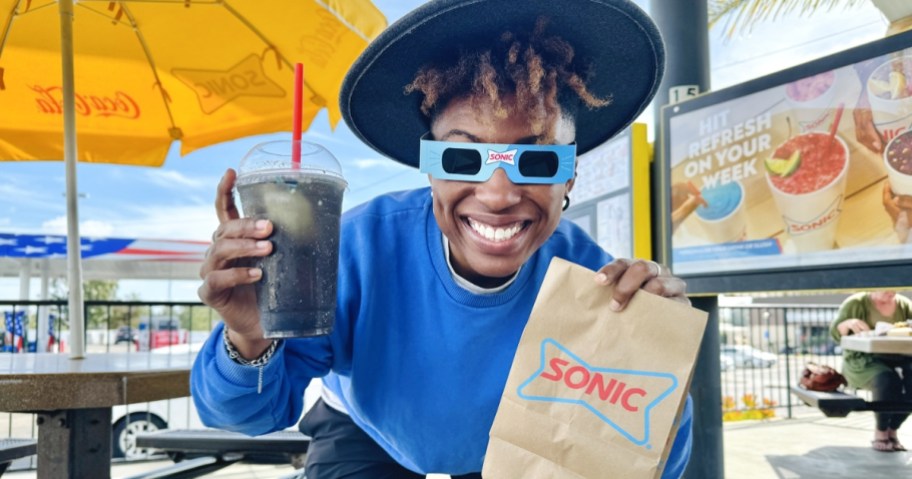 woman wearing sonic eclipse glasses holding bag and blackout slush, one of the best food deals from sonic