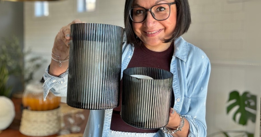 a woman with brown hair and glasses holding up to grey color ribbed glass hurricane candle holders