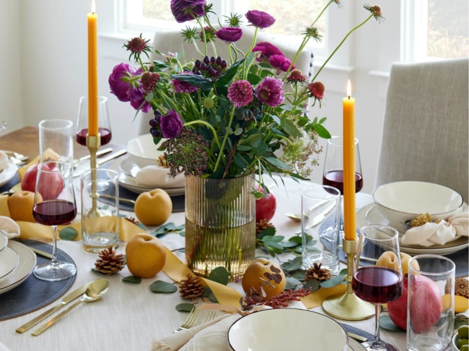 a dinging <a href='https://www.hlc.com.hk/en/the-bathroom-wash-room-area.html' target='_blank' rel='follow'>room</a> table with place settings and fruit with a large glass ribbed vase / candle holder in the middle as a centerpiece with purple wildflowers in it” width=”912″ height=”684″></p>
<div class=