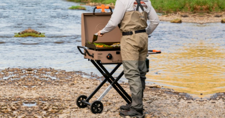 man cooking outside by river on blackstone griddle