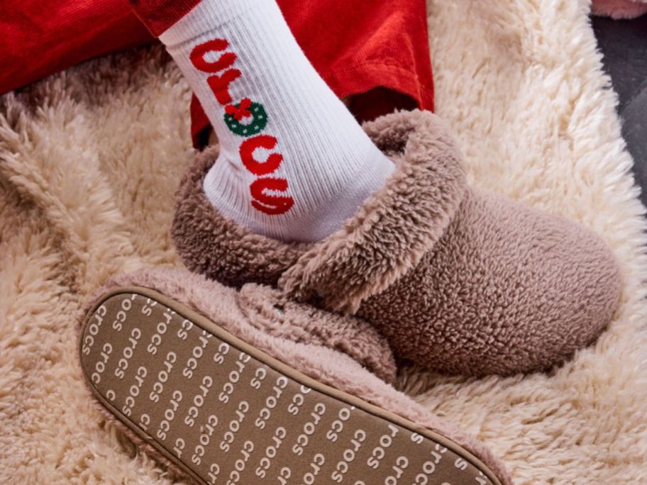 A person wearing Crocs Adult Classic Cozzzy Slippers on a fuzzy rug