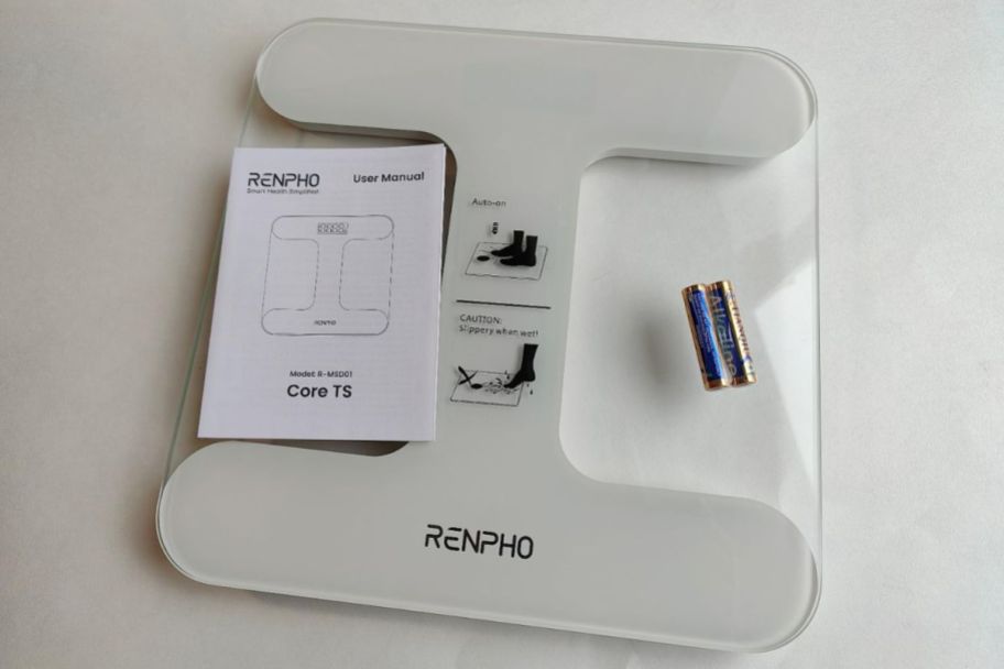 a glass bathroom scale shown with user manual and two AAA batteries