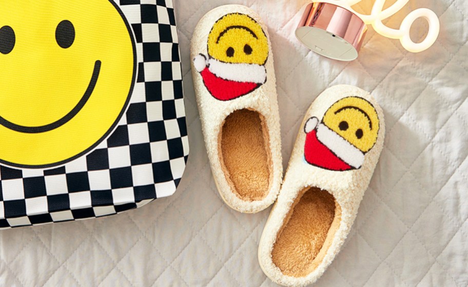 pair of santa smiley face slippers next to a smiley face bag