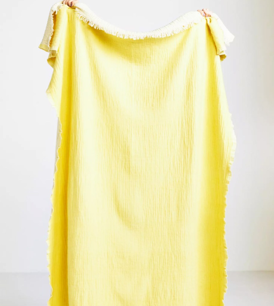 person holding up a yellow throw blanket