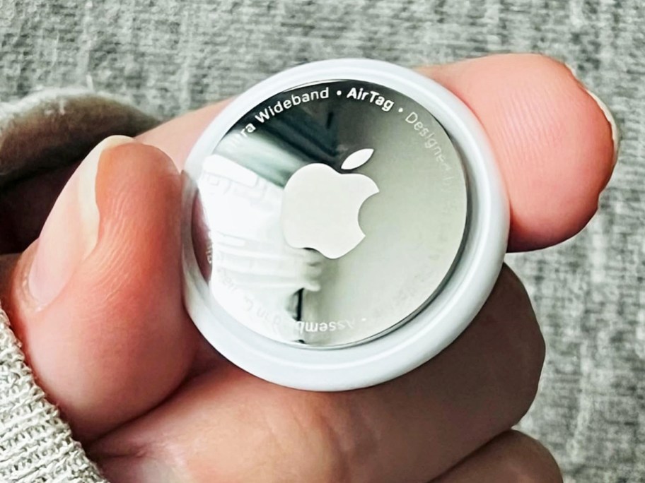 hand holding a silver and white apple airtag