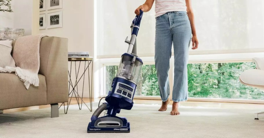 woman using a blue Shark vacuum to vacuum the floor in a living room