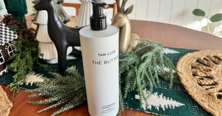 A Bottle of Tan Luxe the Big Butter Self Tanner surrounded by holiday greenery