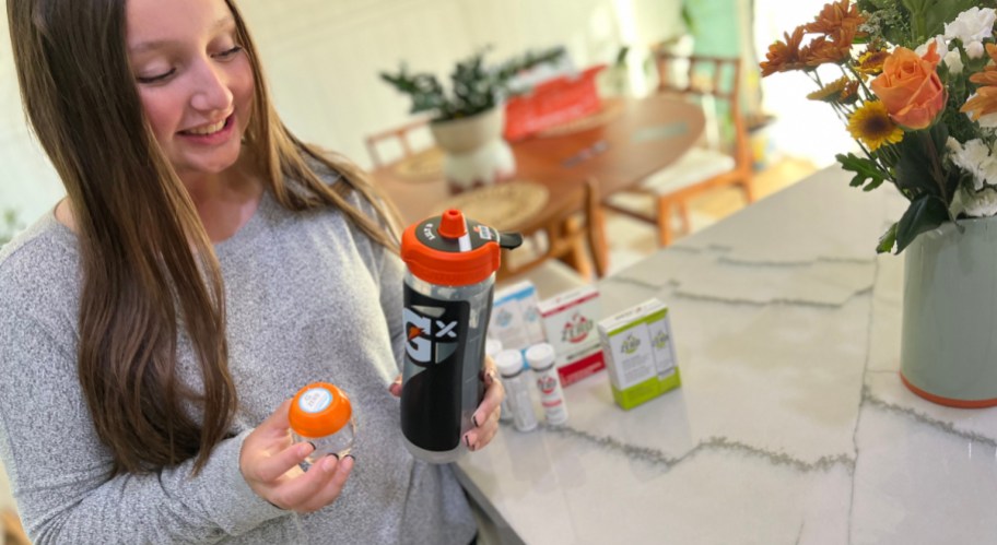 smiling girl holding a gatorade gx water bottle with a personalized lid, with gatorade packets, pods, and tablets in the background