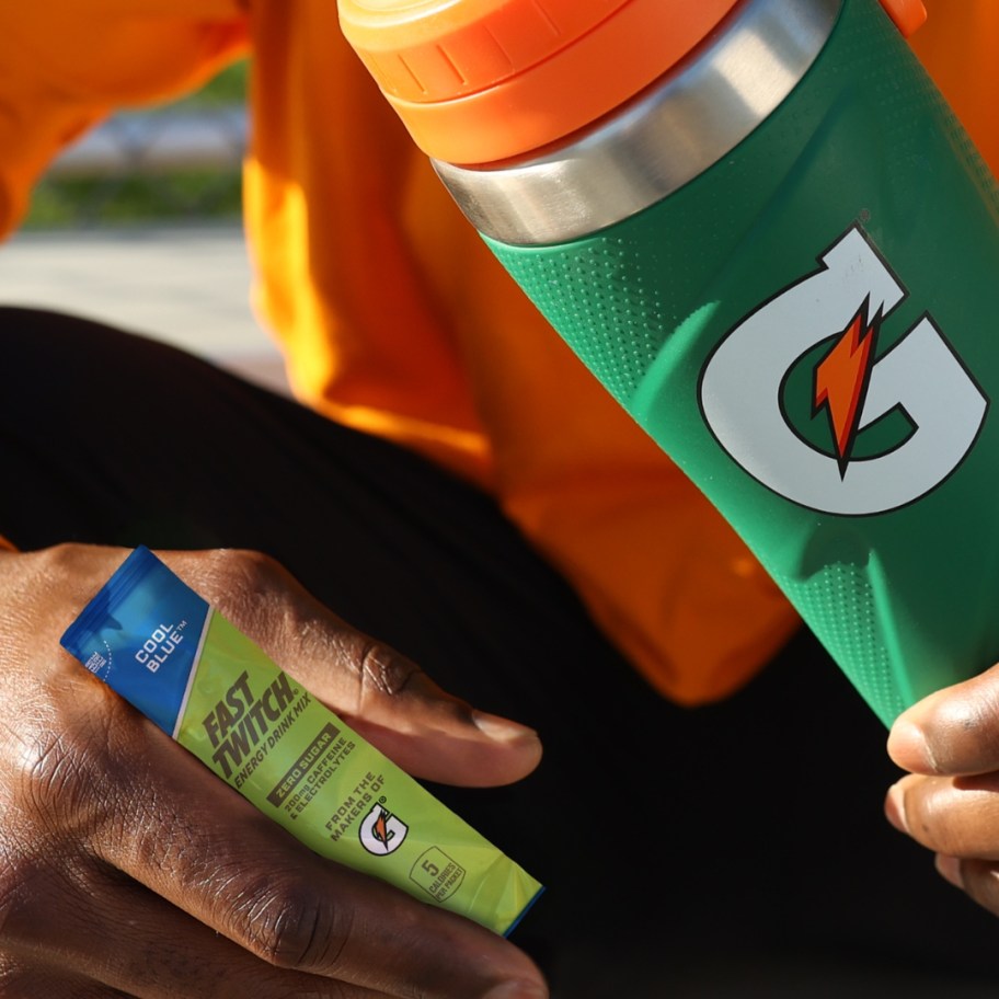 hand holding a single packet of Gatorade Fast Twitch Powder and other hand holding a green and orange Gatorade Stainless Steel Water Bottle