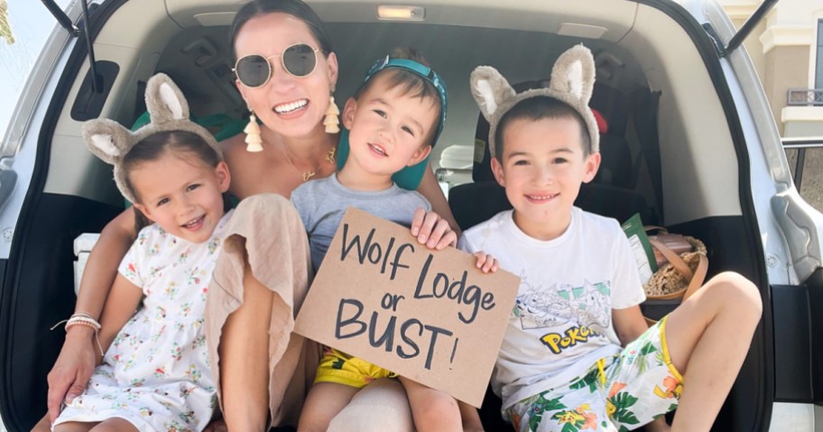 family in trunk of car holding sign