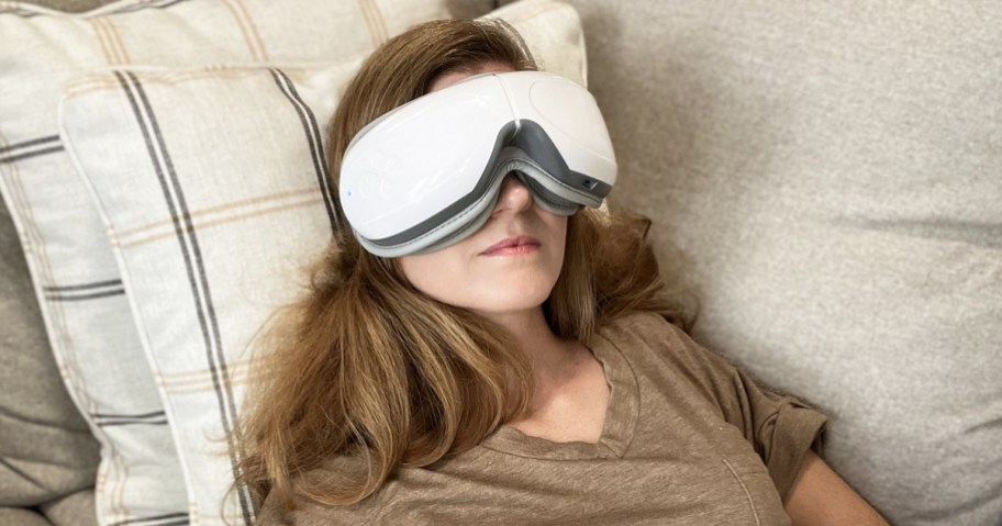 woman laying on couch wearing a white eye massager