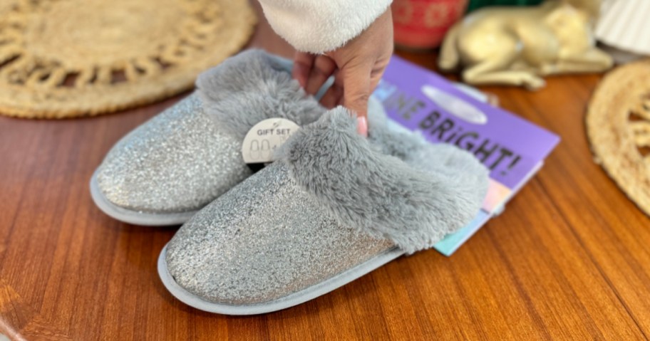 woman holding pair of silver glitter slippers