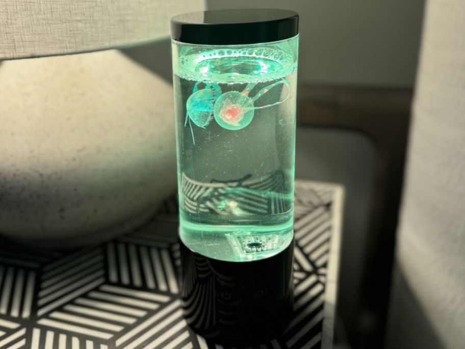 A green Merkury Innovations Jellyfish Lamp on a bed side table