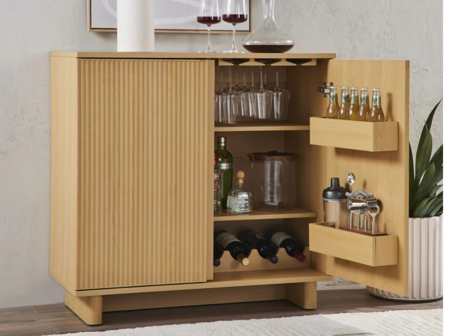 a light tone fluted wood style bar accent cabinet with 1 door open showing glasses and alcohol bottles