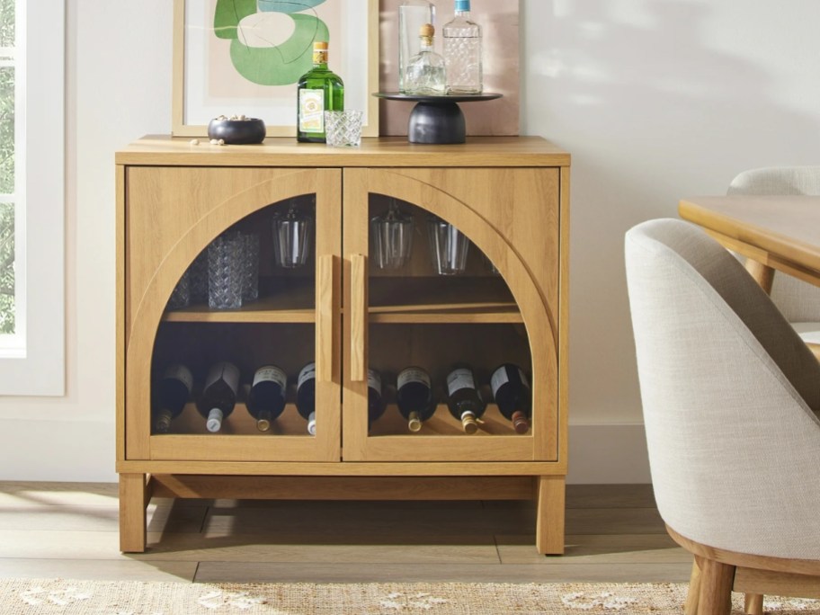 a light wood tone accent cabinet with arched glass doors being used as a bar cabeint