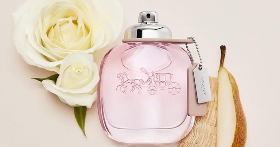 pink bottle of coach perfume near white roses and pear slices