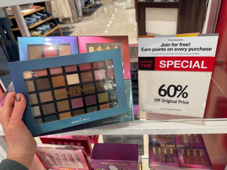 hand holding a beauty makeup palette in a blue box, more behind it with a sign that says 60% off