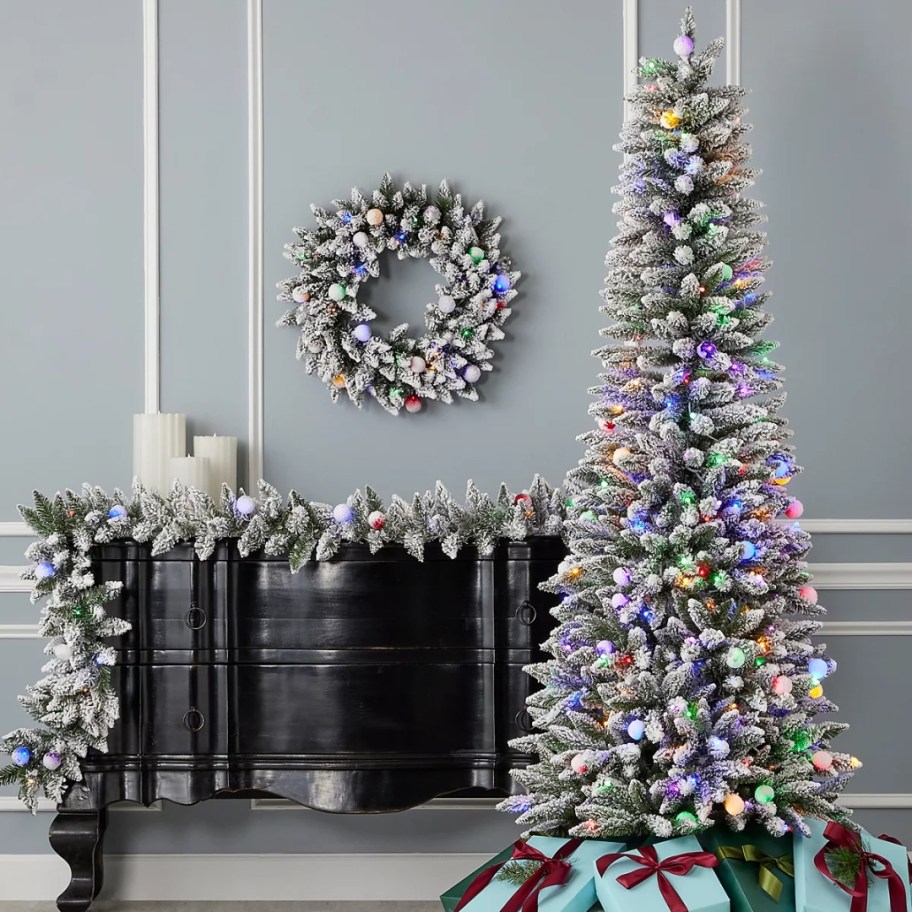 a white flocked green artificial Christmas tree with lights in a living room with matching wreath and garland over a mantle