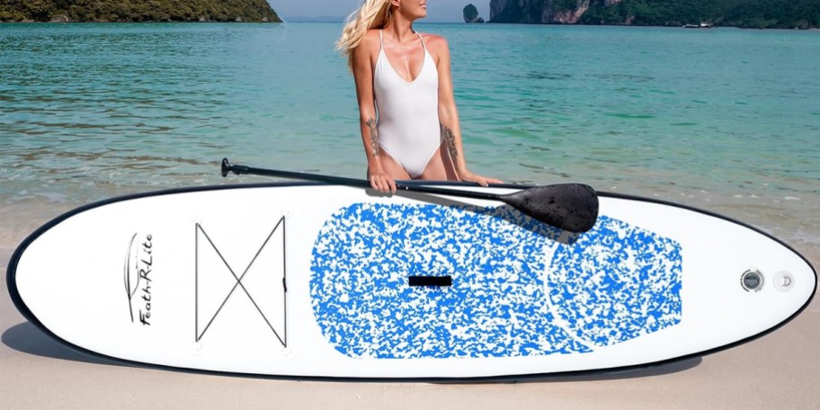 woman holding white and blue paddleboard next to beach