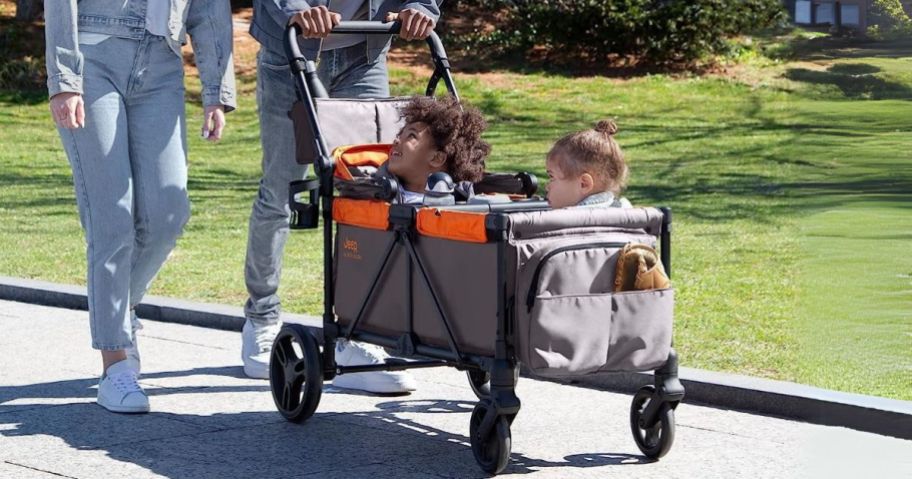 man pushing Delta Children Store Jeep Wrangler Sport All-Terrain Stroller Wagon in park