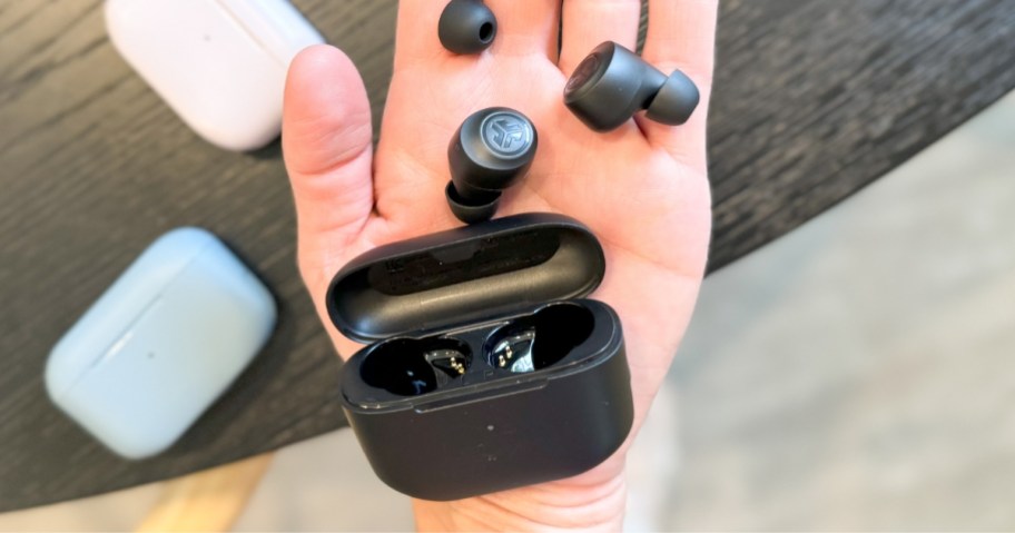 hand holding small black Jlab earbuds and a black charging case, plus extra ear pieces