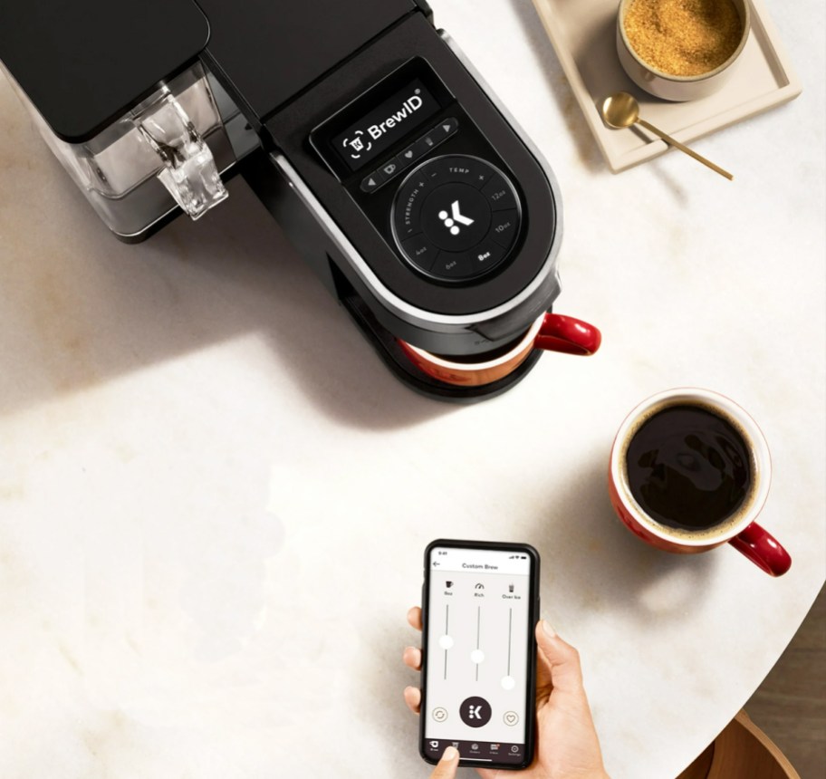 person using phone to brew cup of coffee from keurig