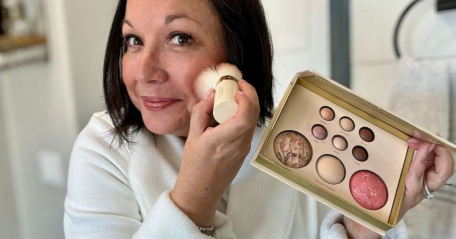 Woman applying Laura geller makeup from a palette using a kabuki brush