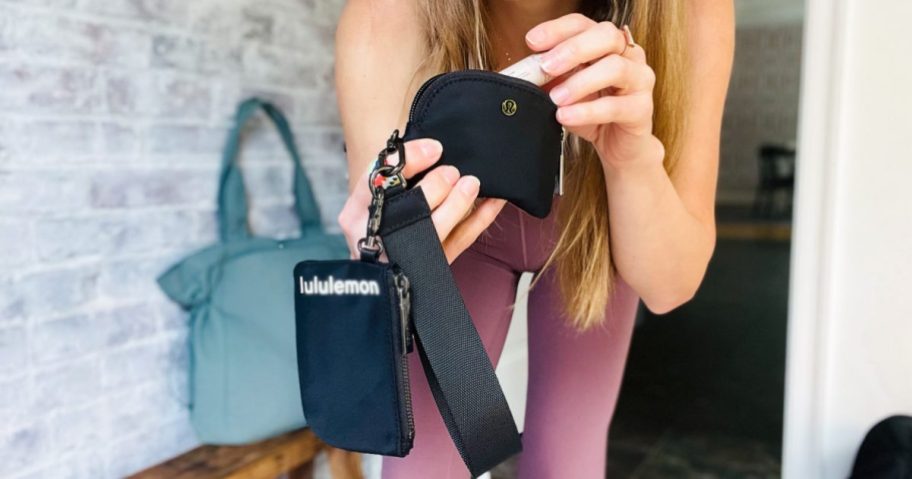 Woman putting lip gloss into Lululemon Wristlet in black