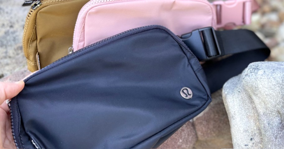 Hand holding a black lululemon belt bag that is sitting on other belt bags.