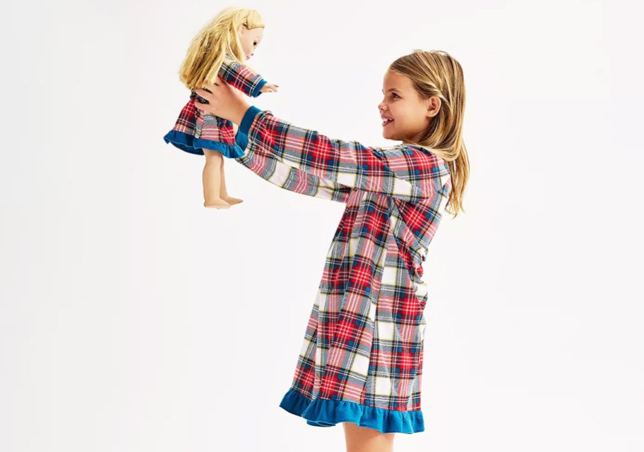 girl holding up a doll in matching plaid nightgowns