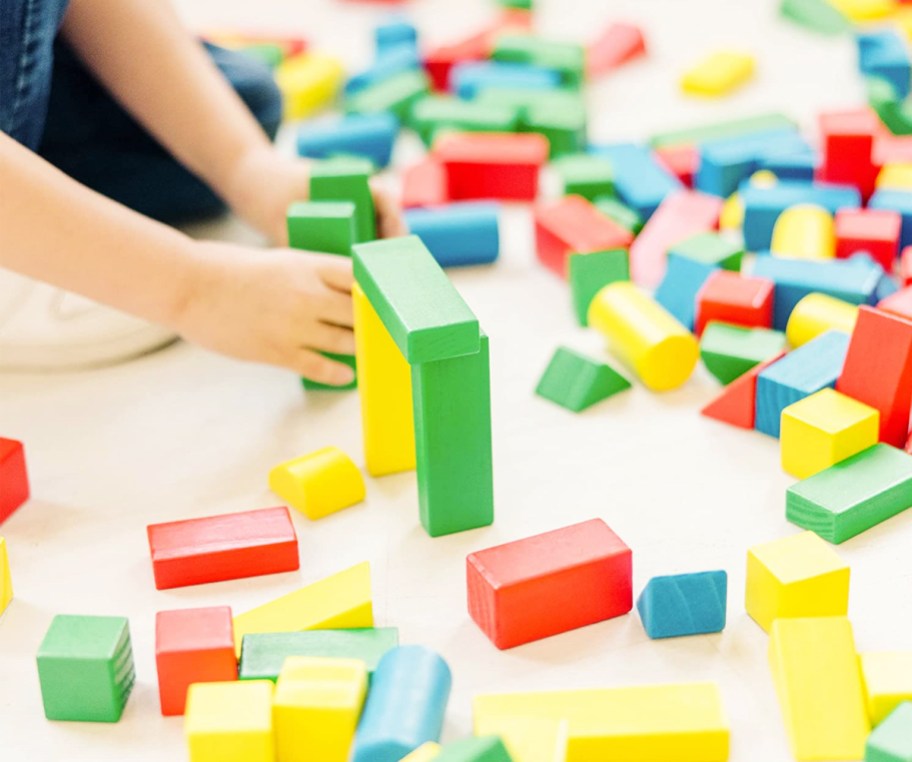 child playing with red, blue, yellow, and green wooden building blocks