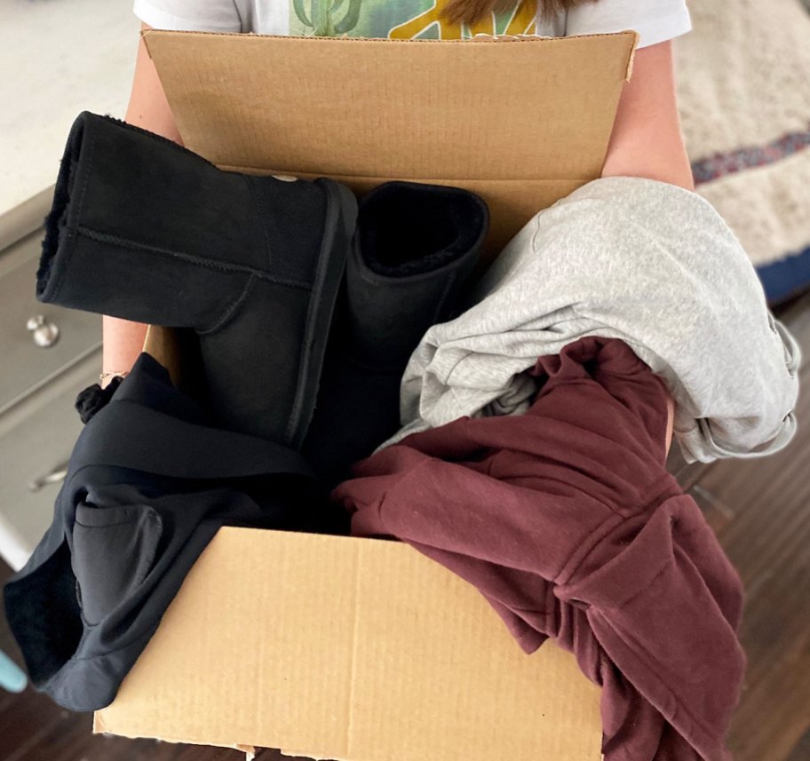 person holding up a brown shipping box full of pieces of clothing and pair of <a href='https://shopsimart.com/product/cordless-digital-jump-rope-for-fitness-and-calorie-tracking' target='_blank' rel='follow'>black</a> boots” width=”912″ height=”857″></p>
<p>Through December 24th and while supplies last, RUN over to <a href=