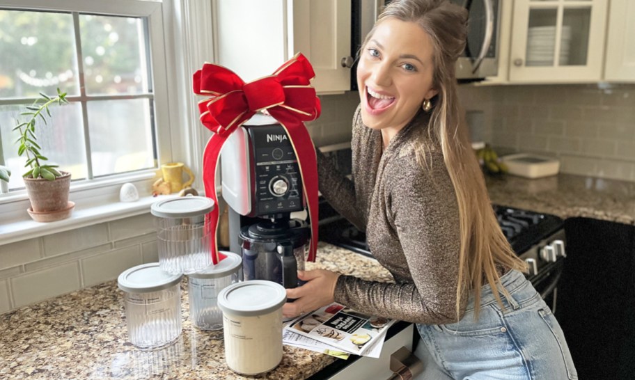 woman next to a ninja creami machine with a red bow and extra pint containers