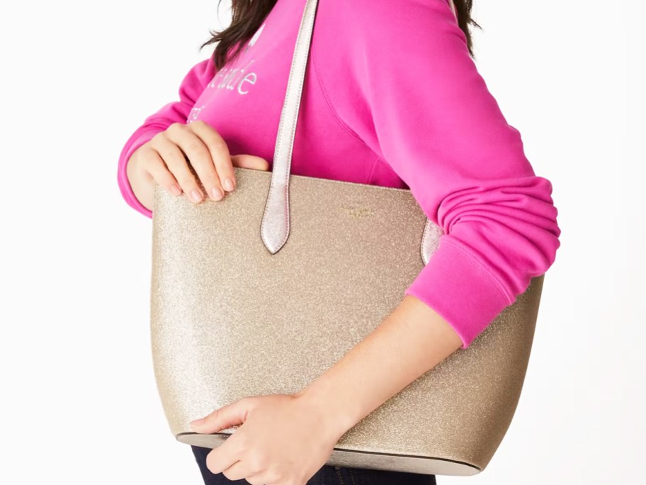 woman in a pink sweatshirt with a glittery gold tote bag