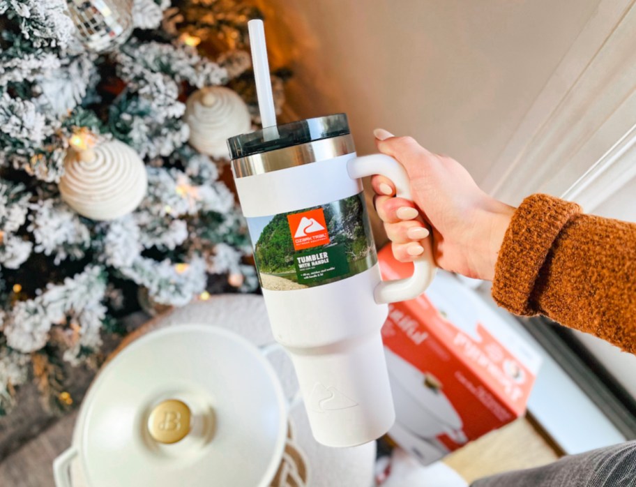 hand holding white ozark trail tumbler in front of christmas tree