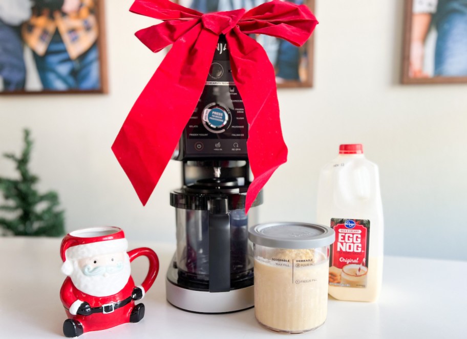 ninja CREAMi ice cream maker sitting on countertop with egg nog santa cup and giant red bow